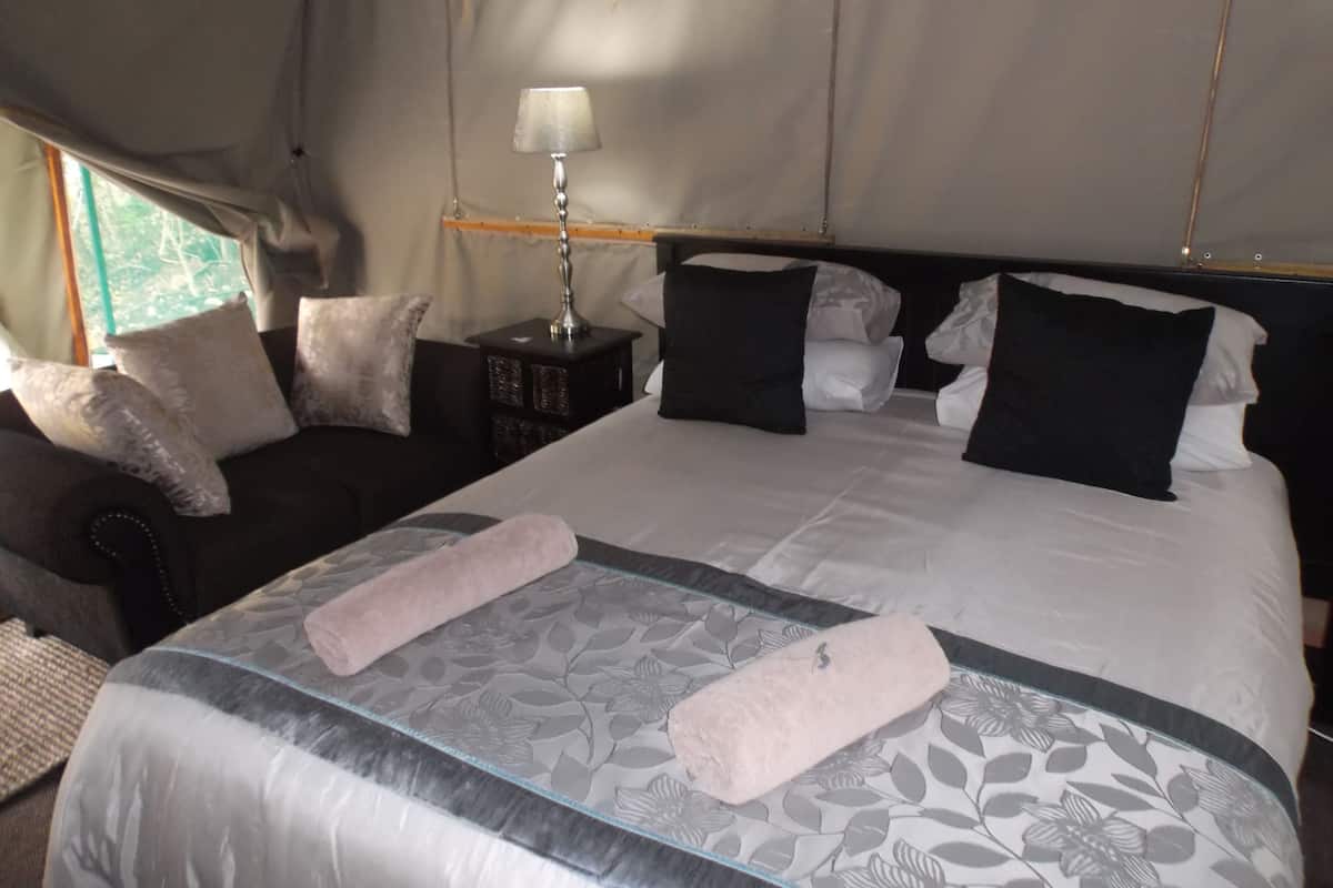 Een slaapkamer met een bed, kussens, een nachtkastje, een lamp en een raam.