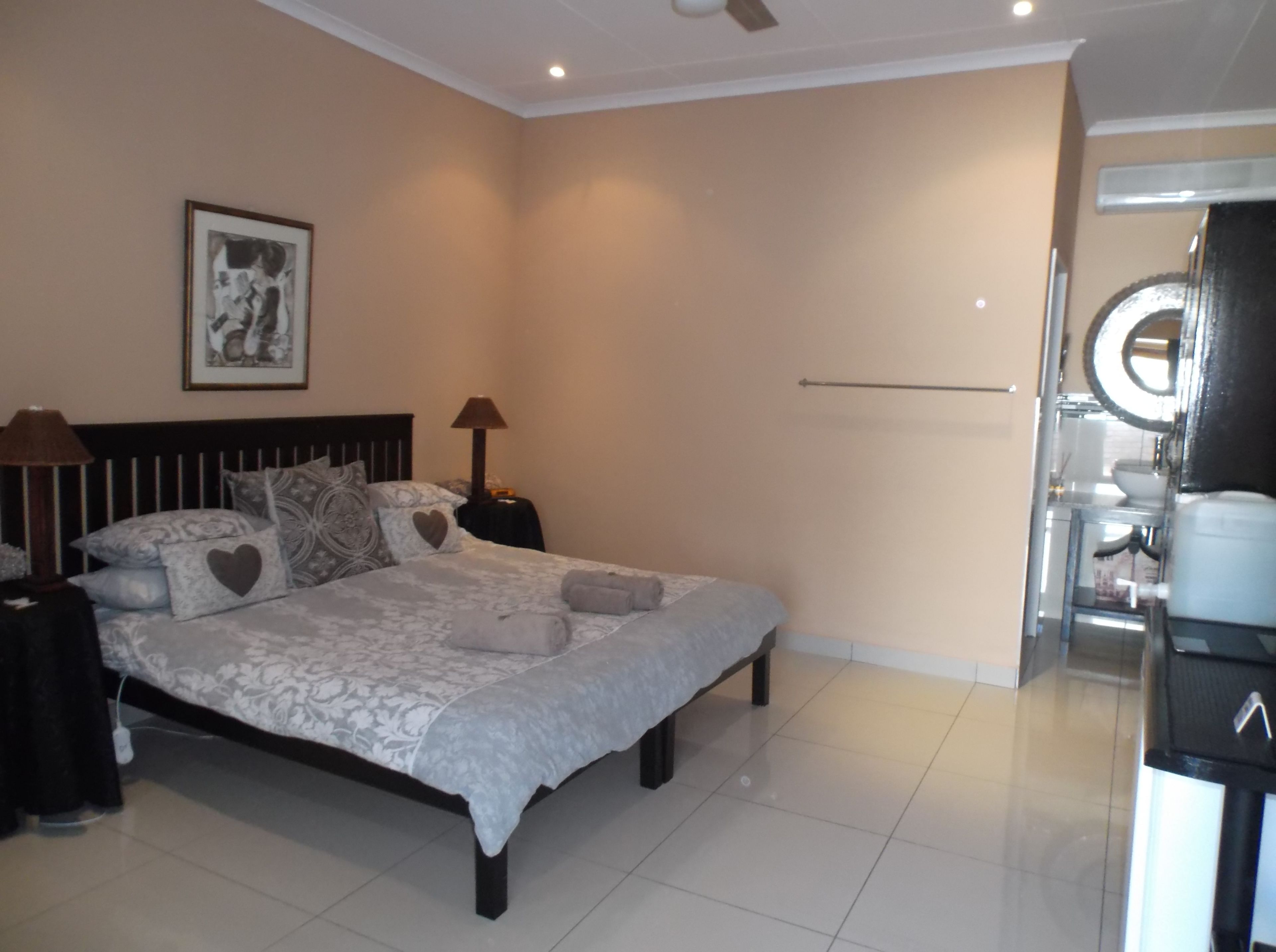 A bedroom with a bed, bedside lamps, a framed picture on the wall, and a bathroom visible through an open door.