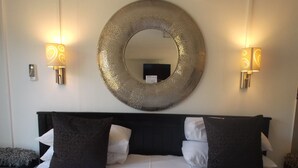 Une chambre d’hôtel avec un grand lit, deux lampes fixées au mur, un miroir rond et un appareil de climatisation.