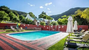 Une piscine entourée de chaises longues et de parasols, elle-même bordée d’une terrasse en briques et d’un mur rouge.