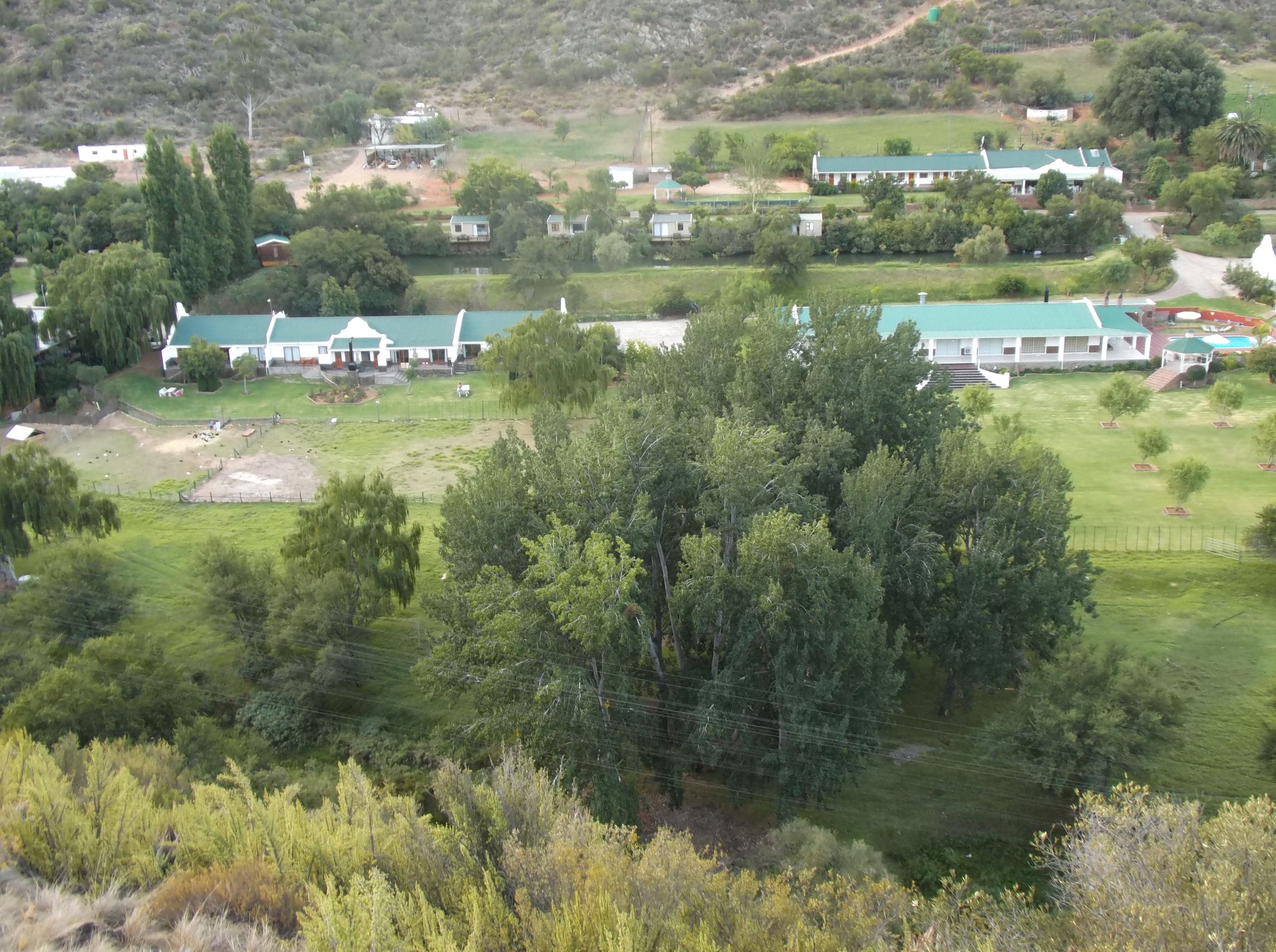 A rural area with several buildings, including a large house with a green roof and smaller structures. There are trees and open fields visible.
