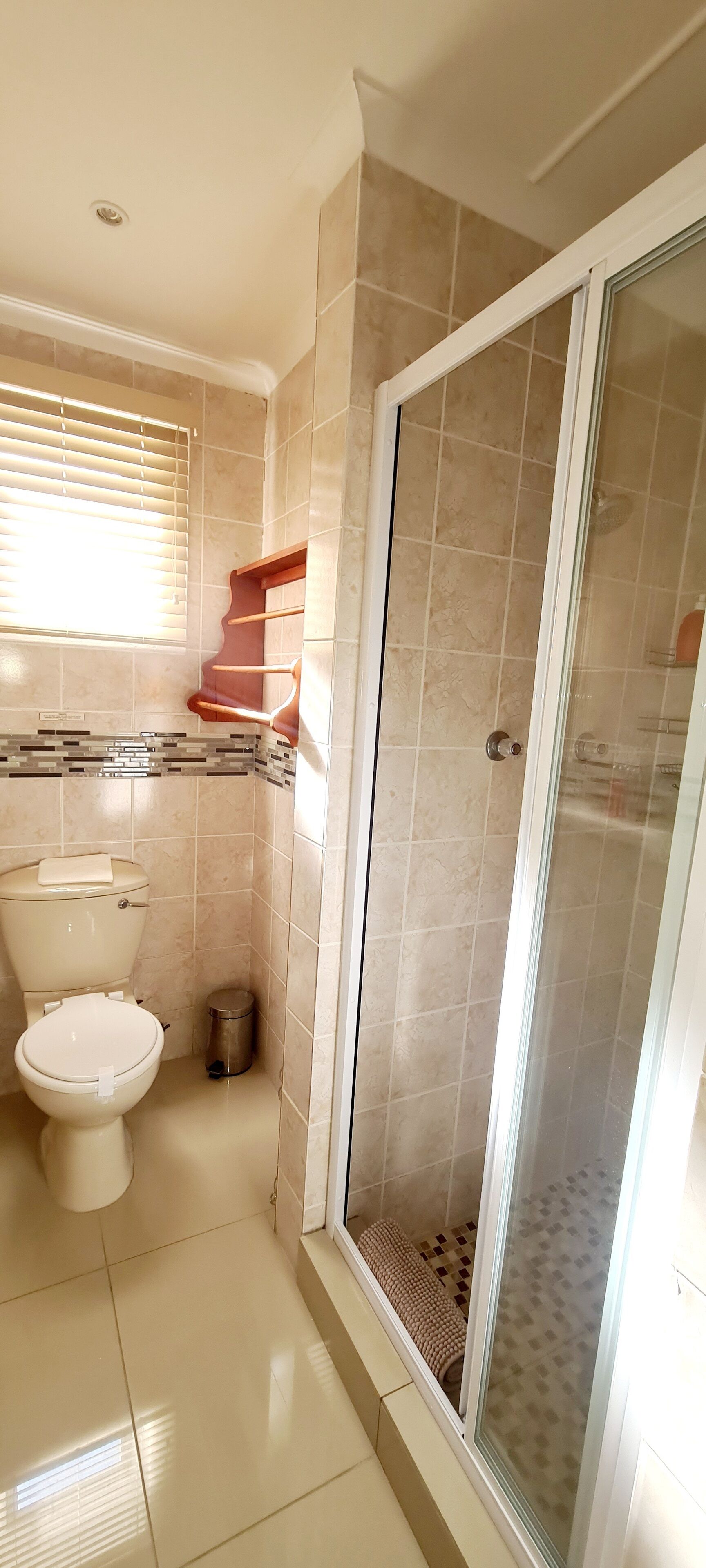 Une salle de bain comprenant des toilettes, une douche avec une porte en verre et une fenêtre avec des stores.