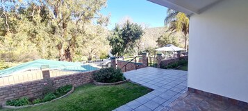 A backyard with a swimming pool, a covered patio, and a brick wall.