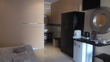 Habitación de hotel compacta con cama, kitchenette, refrigerador, cafetera y una pequeña mesa.