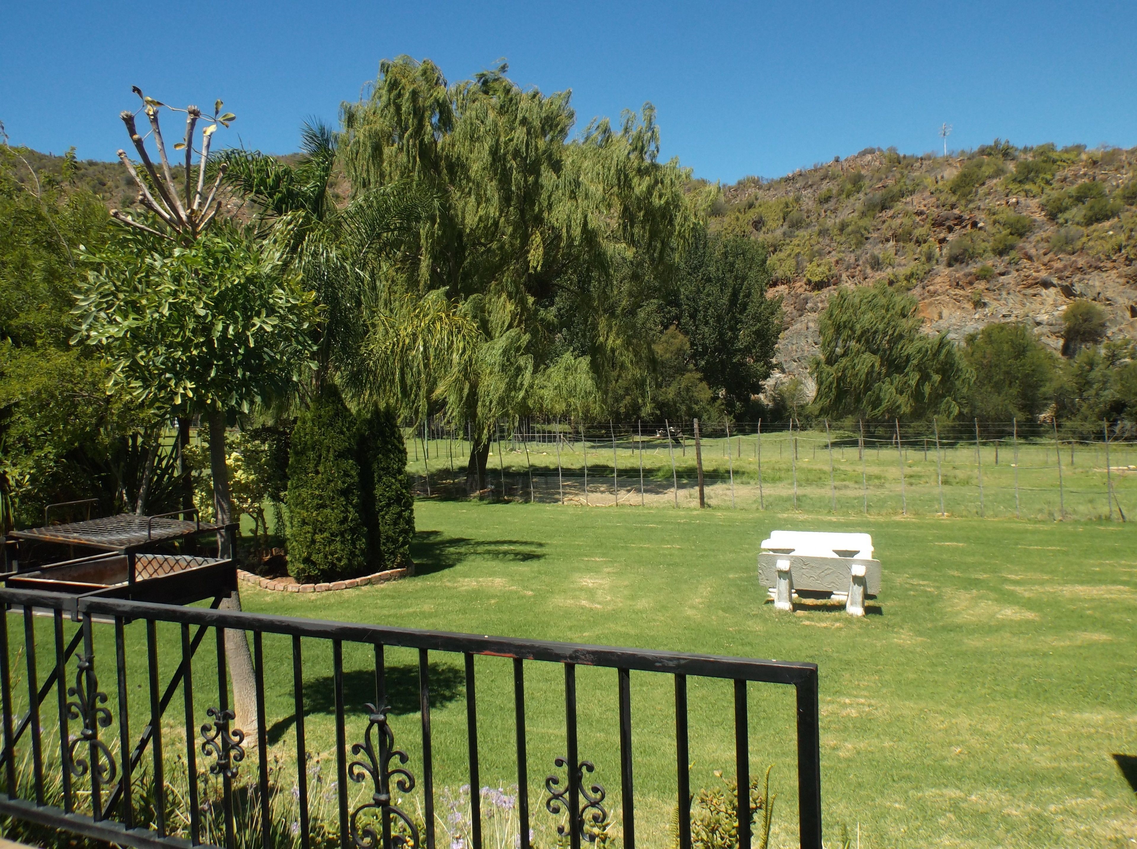 A grassy outdoor area with a metal fence, a stone bench, and a white table.