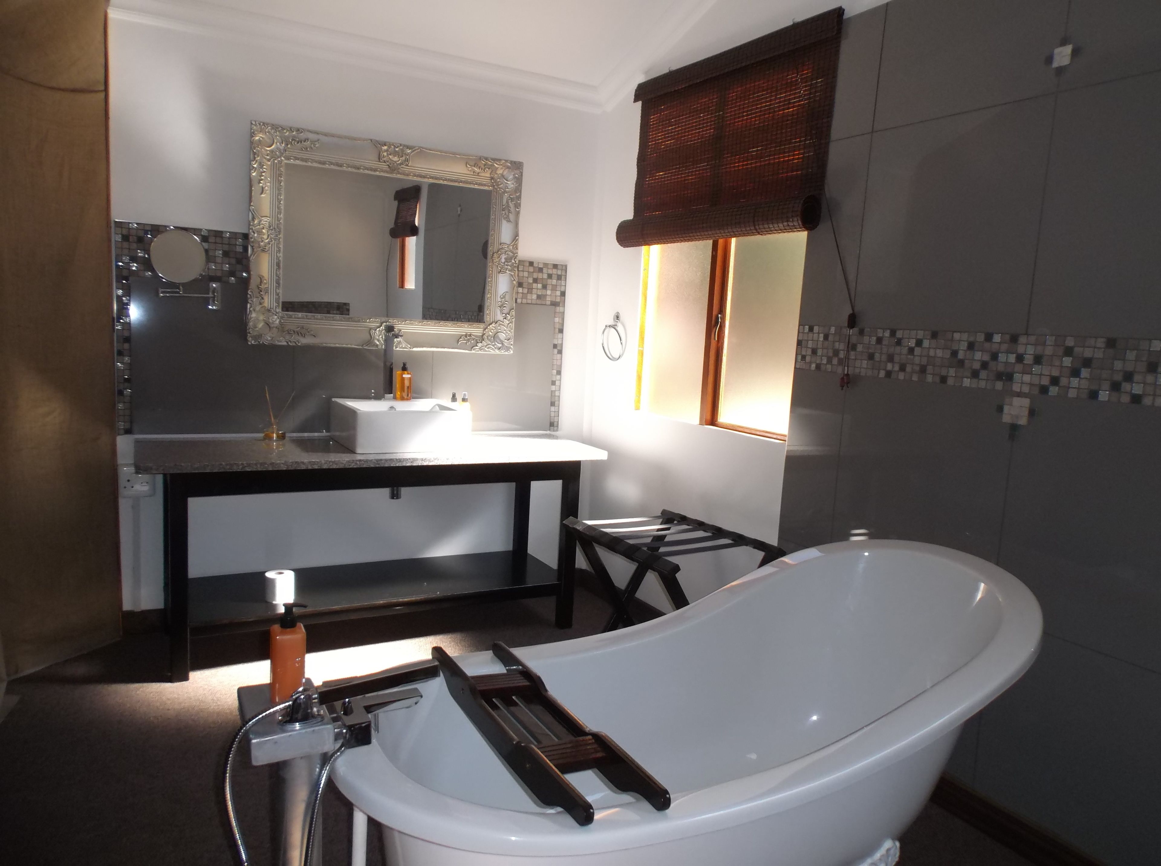 Une salle de bain avec une baignoire sur pieds, un meuble-lavabo avec un miroir et une fenêtre avec un store.