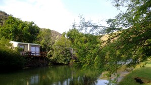 Un chalet au bord de la rivière, doté d’une terrasse en bois et d’un petit pont.