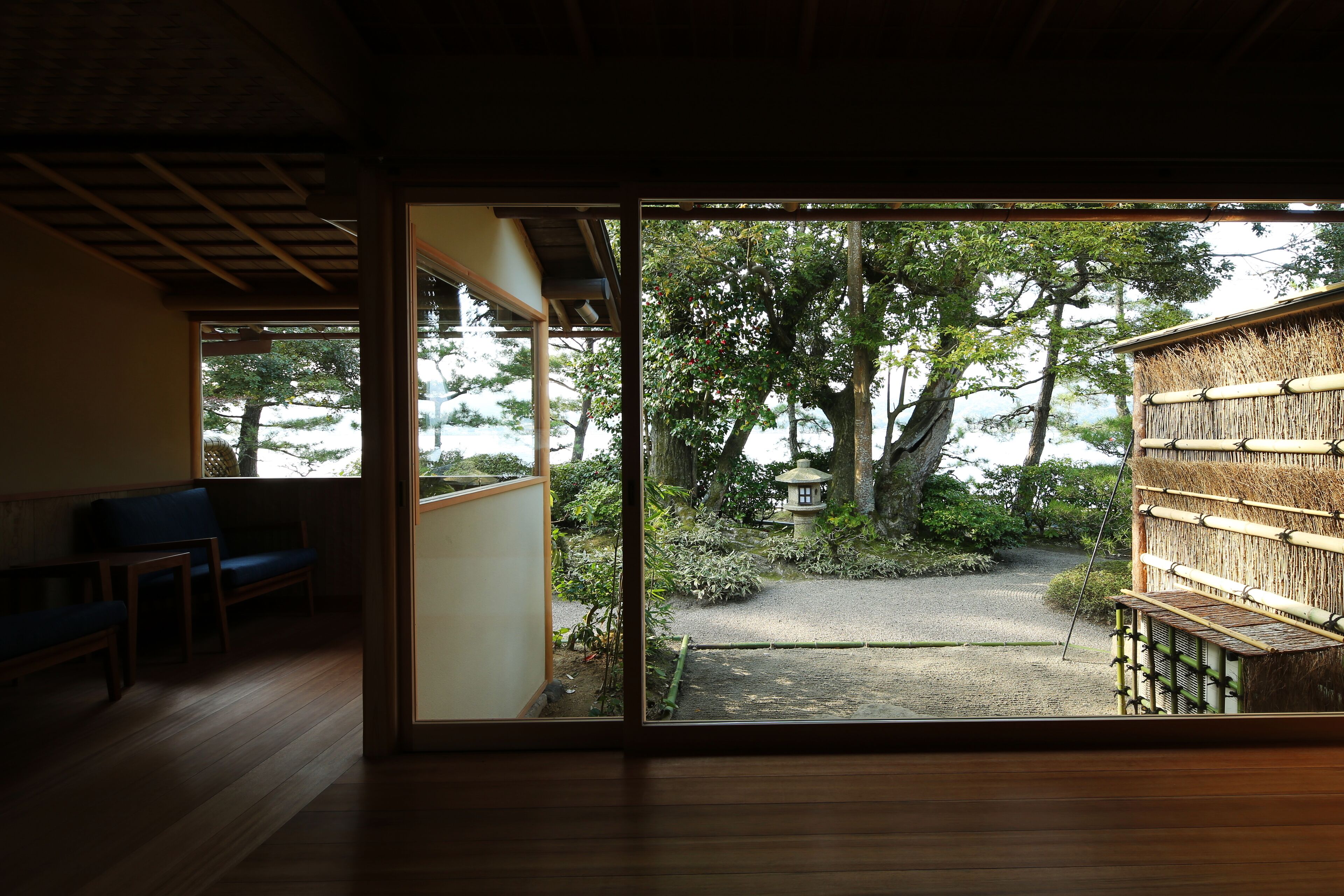 A traditional Japanese room with tatami flooring, a sliding door leading to a garden with a stone lantern and bamboo fence.