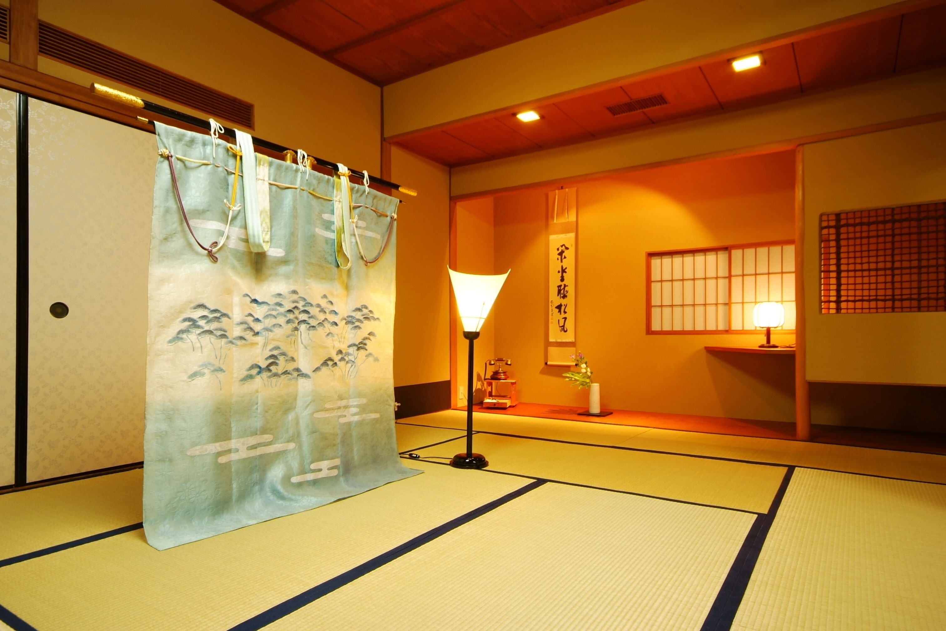 A traditional Japanese room with tatami flooring, a shoji screen, and a hanging shimenawa.