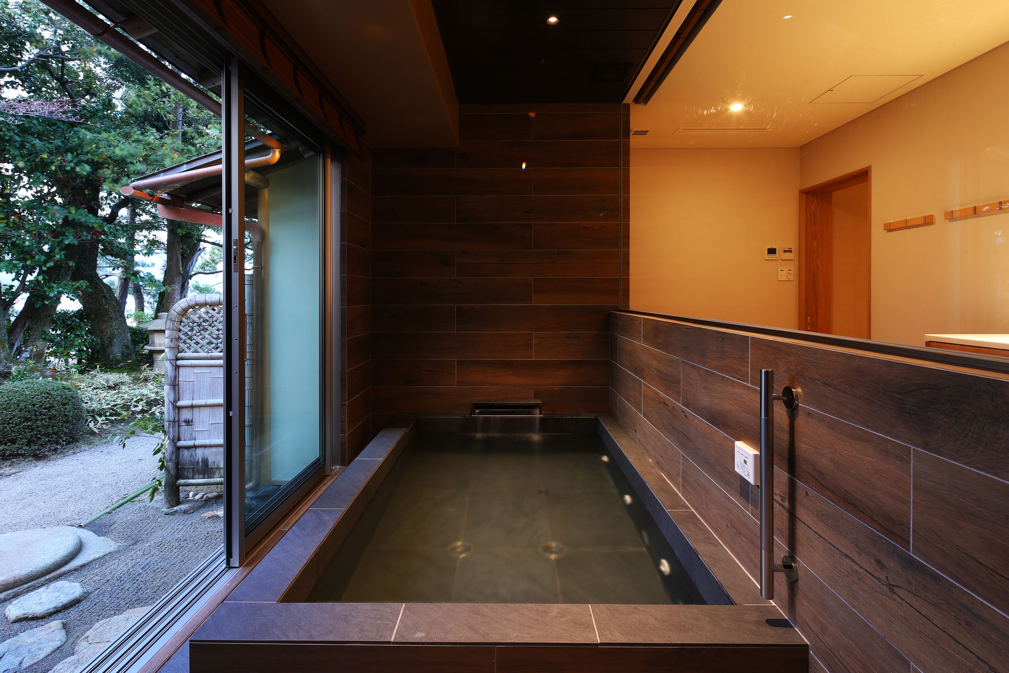 Un baño moderno con detalles de madera, cabina de ducha de vidrio y vista a un jardín exterior.