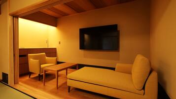 Una sala de estar moderna con un sofá, una mesita y una silla. Tiene piso de madera y un televisor montado en la pared.