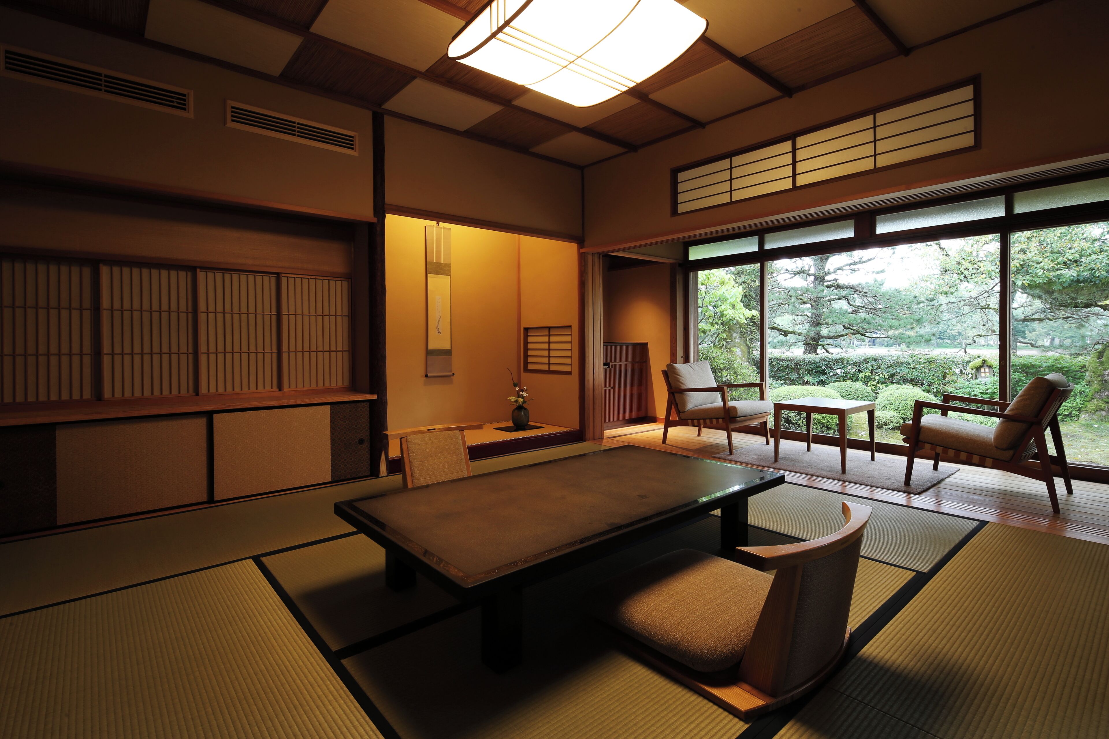 A traditional Japanese room with tatami flooring, a low table, and a view of a garden through large windows.