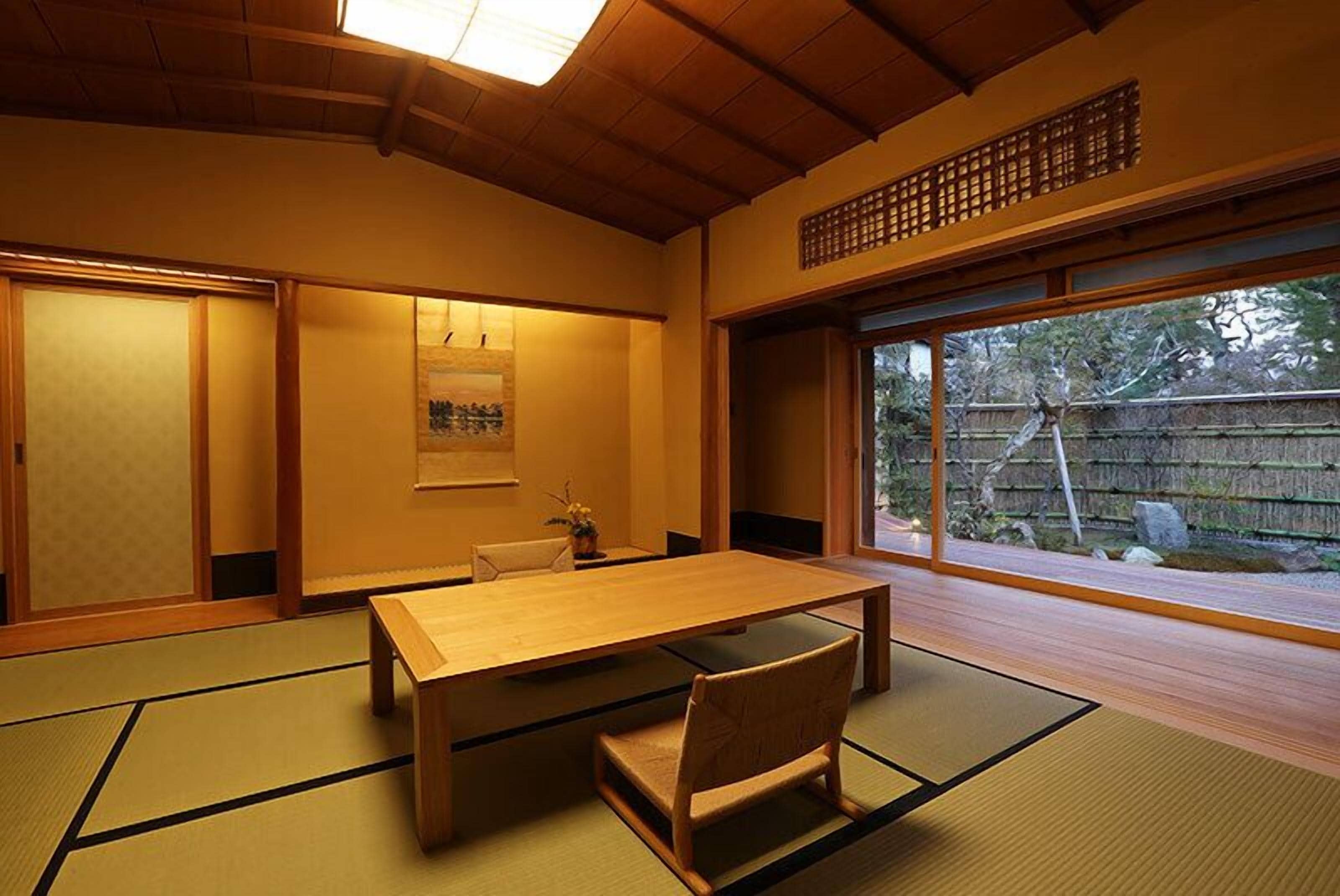 A traditional Japanese room with tatami flooring, a wooden table, a chair, sliding doors, and a view of the outdoors.