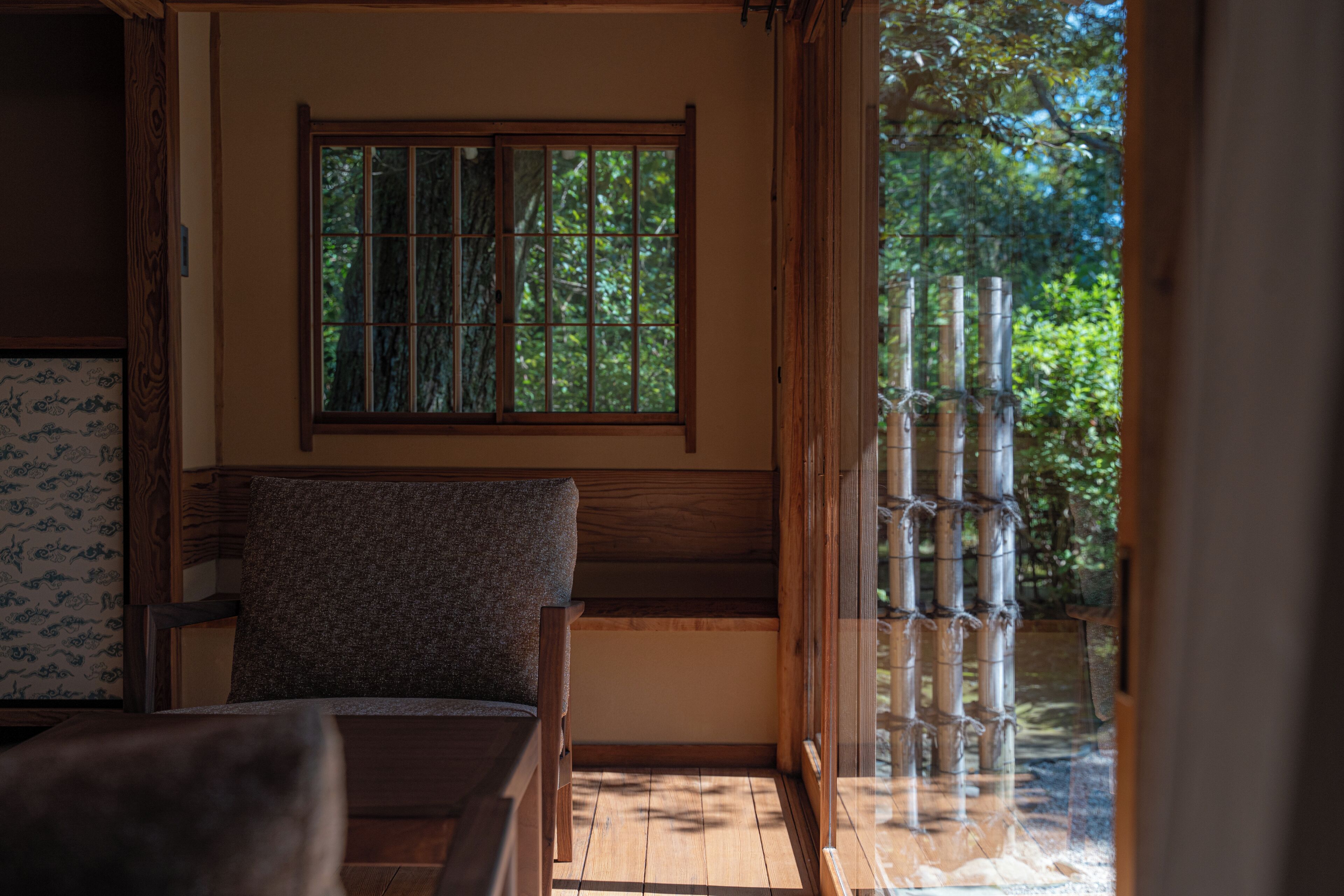 Una habitación con un banco de madera, una ventana que da a vistas de bambú y un muro con diseño.
