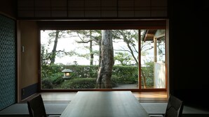 Une pièce de style japonais traditionnel, avec un sol recouvert de tatamis, une table basse et une vue sur un jardin, accessible par une porte coulissante.
