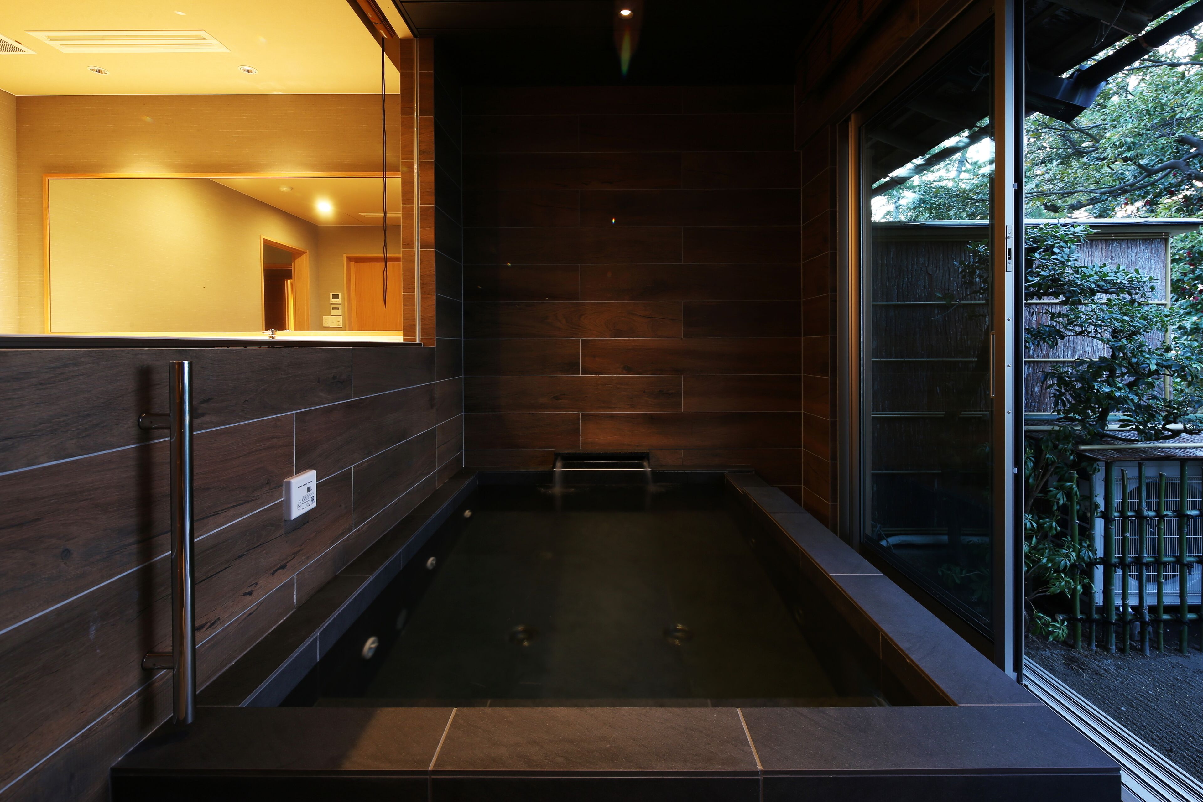 A modern bathroom with a large bathtub, wooden walls, and a view of the outdoors.