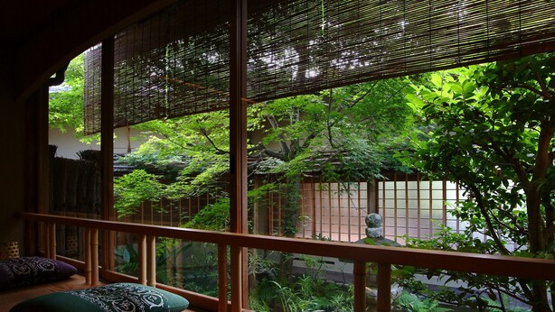 Une pièce de style japonais traditionnel, avec un sol recouvert de tatamis, un banc en bois agrémenté de coussins et une vue sur un jardin luxuriant, visible à travers un paravent shoji.