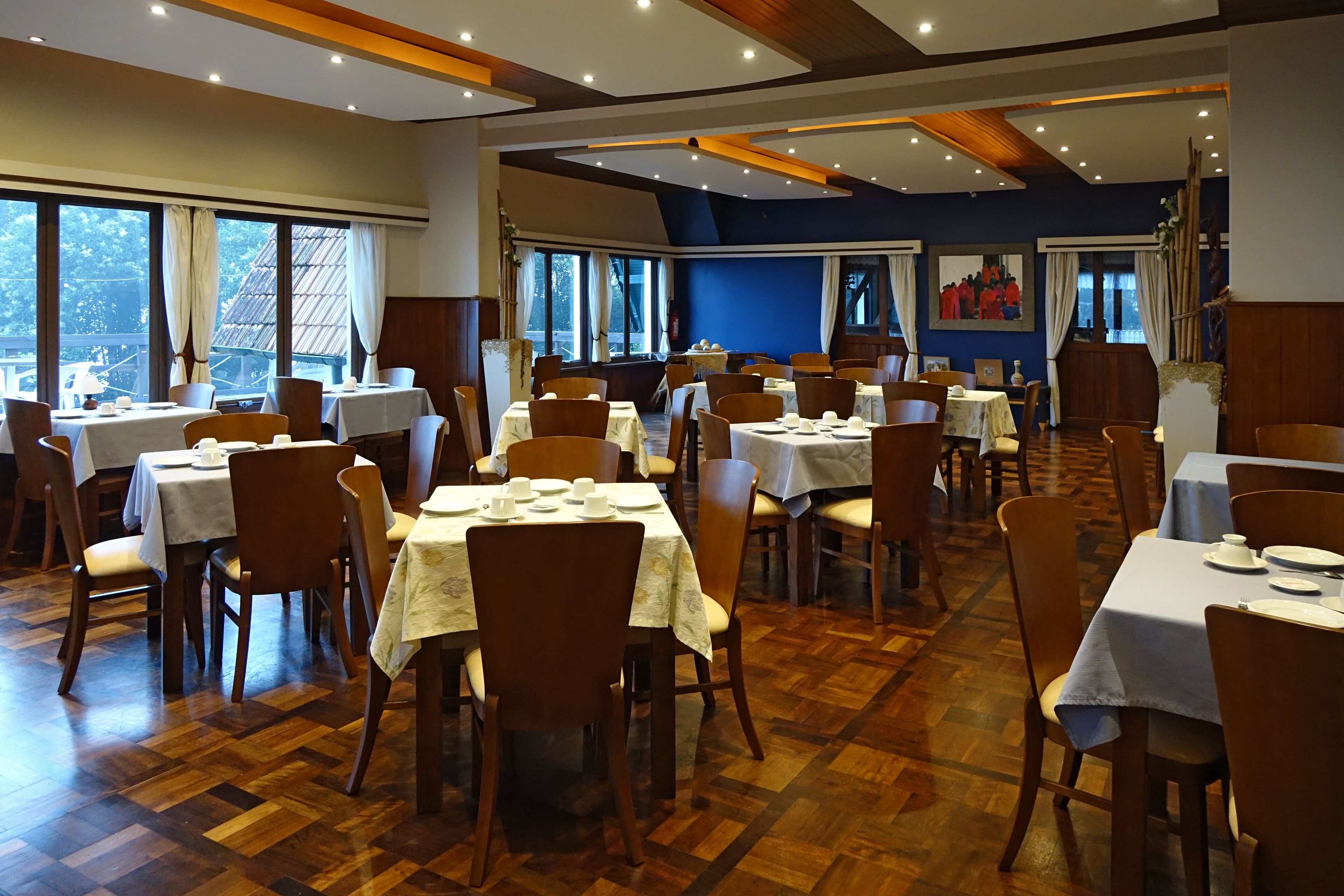 A restaurant with multiple tables and chairs, large windows, and a wooden floor.