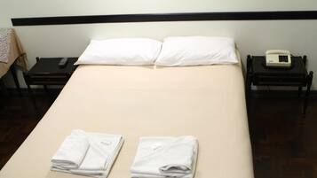 Cama bem arrumada com duas toalhas dobradas, um controle remoto e um telefone em uma mesinha de cabeceira.