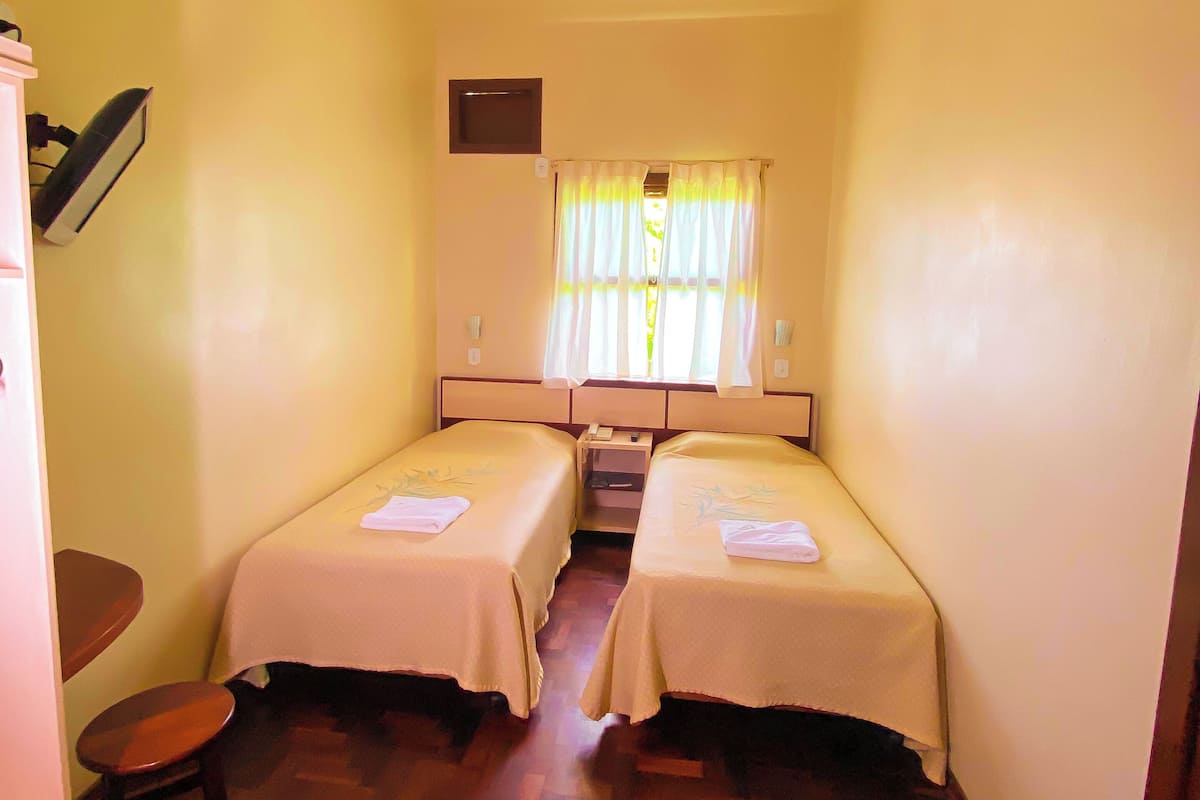 A small, narrow room with two single beds, a desk, and a chair.