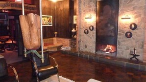 A cozy lounge area with a stone fireplace, leather seating, and a bar sign in the background. - Hotel Pousada João de Barro (Rio Negrinho)