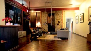 A spacious lobby with a wooden floor, a reception desk, seating area, and a stone wall with a hanging sculpture. - Hotel Pousada João de Barro (Rio Negrinho)