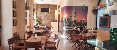 Un restaurante con mesas y sillas de madera, una pared de piedra y un mural del paisaje urbano en la pared de fondo.
