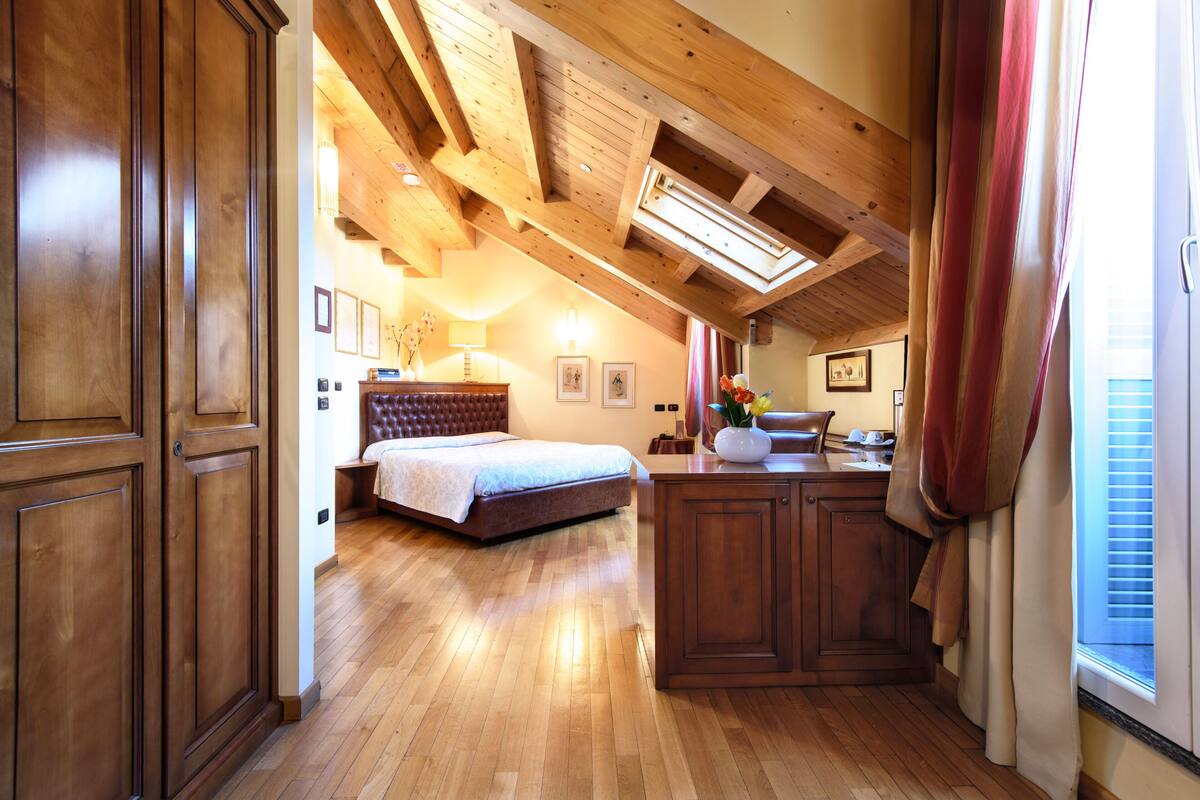 Un dormitorio amplio con una cama grande, vigas de madera en el techo y un tragaluz.