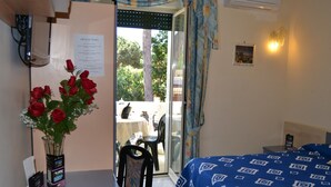 Habitació d'hotel amb un llit, una taula amb un ram de roses vermelles, una cadira i vista a l'exterior a través d'una porta de vidre.