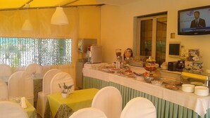 Zona de dinar amb taules i cadires, barra de buffet amb aliments, màquina de cafè i pantalla de televisió que mostra un programa d'informatius.