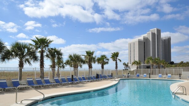 A swimming pool with blue lounge chairs and palm trees, surrounded by a white fence.