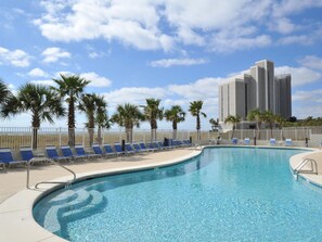 A swimming pool with blue lounge chairs and palm trees, surrounded by a white fence. - Tidewater By Wyndham Vacation Rentals (Orange Beach)