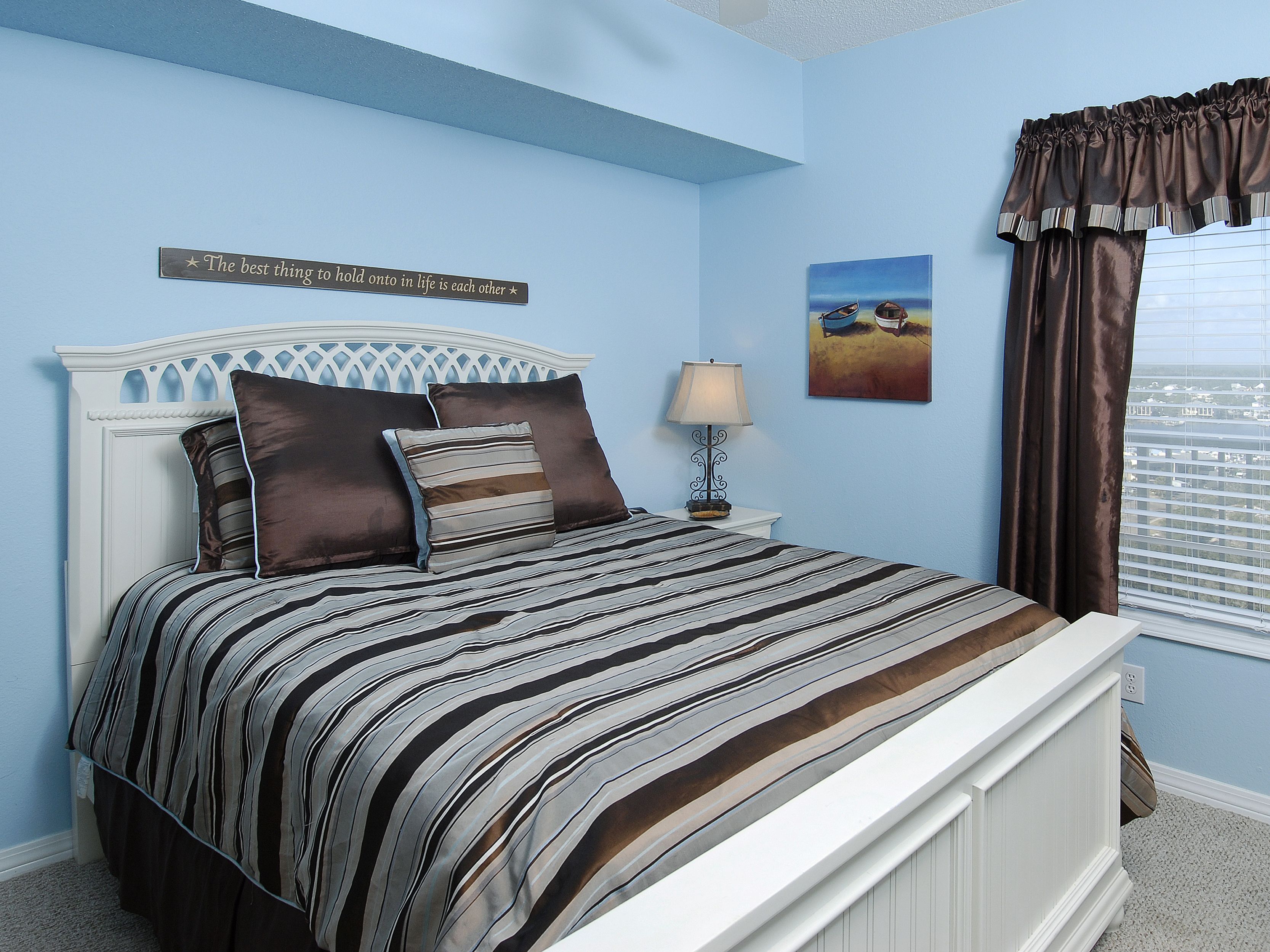 A bedroom with a bed, a nightstand, a lamp, a painting, and a window with curtains.