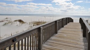 A wooden boardwalk leading to a beach with sand dunes and a clear sky.