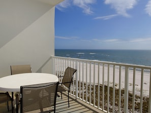 A balcony with a white railing, a round table, and two wicker chairs.