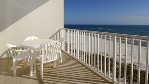 A balcony with a white table and chairs, overlooking a beach with a railing.