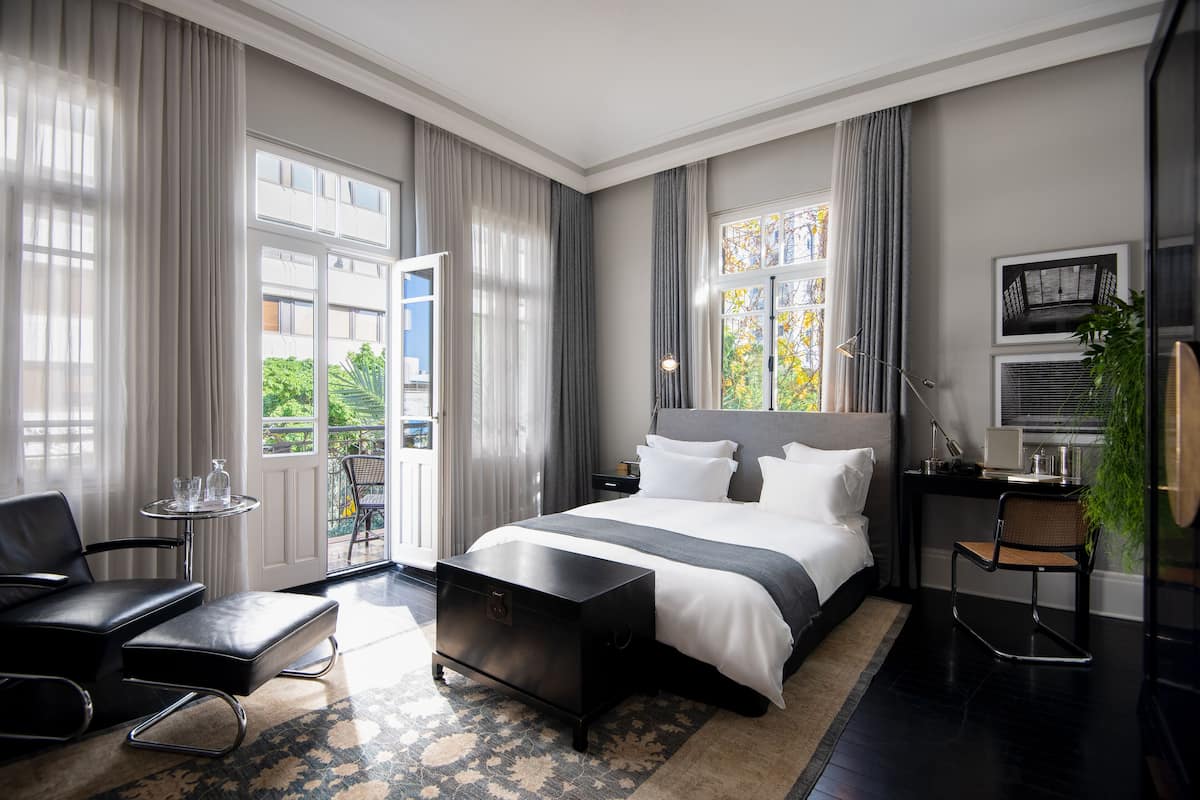 Quarto de hotel moderno com uma cama grande, uma escrivaninha, uma cadeira e uma mesinha.