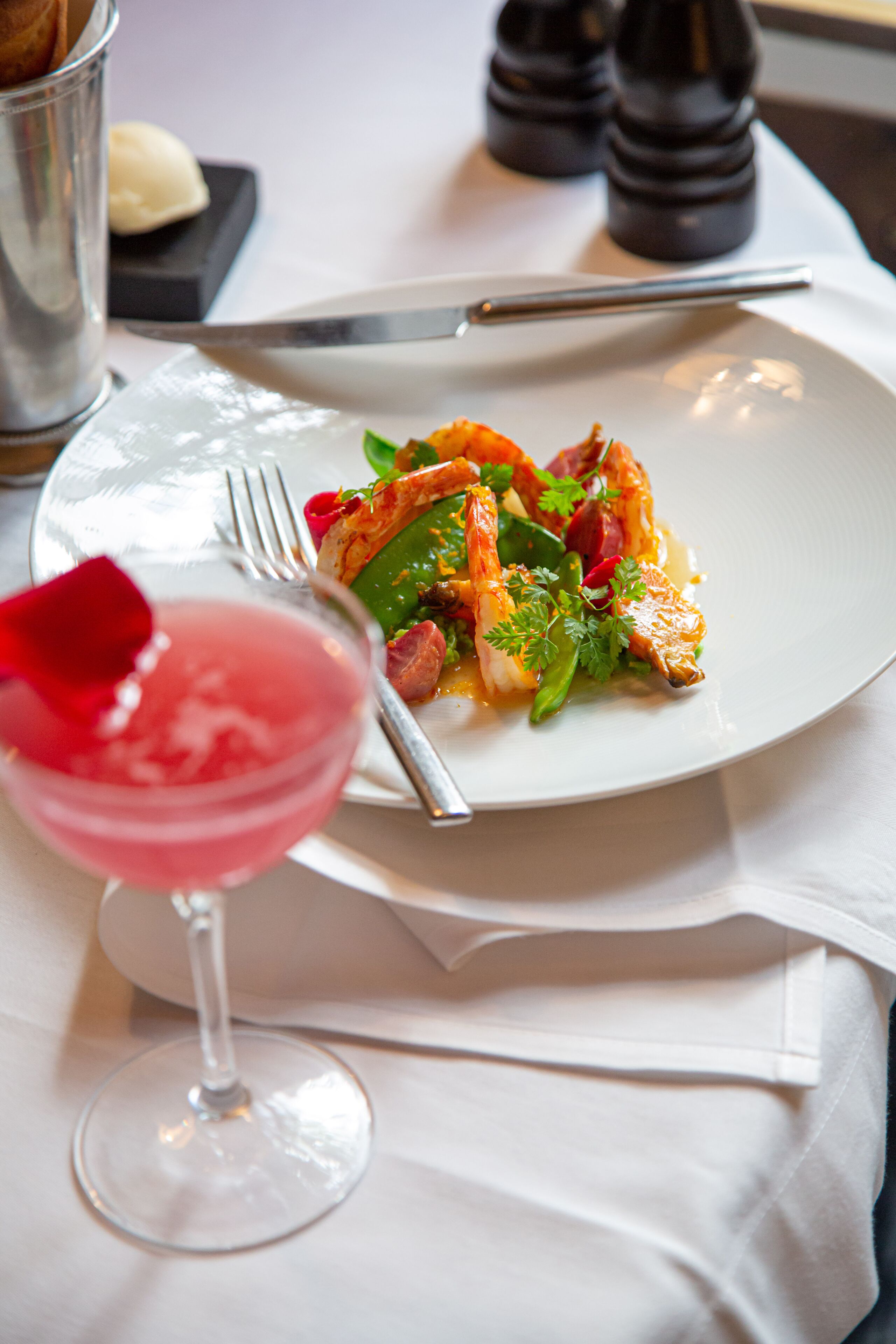 A plate of food with a fork and a glass of pink drink on a table.