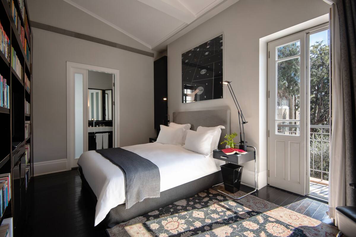 Quarto moderno com uma cama grande, mesa de cabeceira, abajur e vista para o exterior através de uma porta de vidro deslizante.