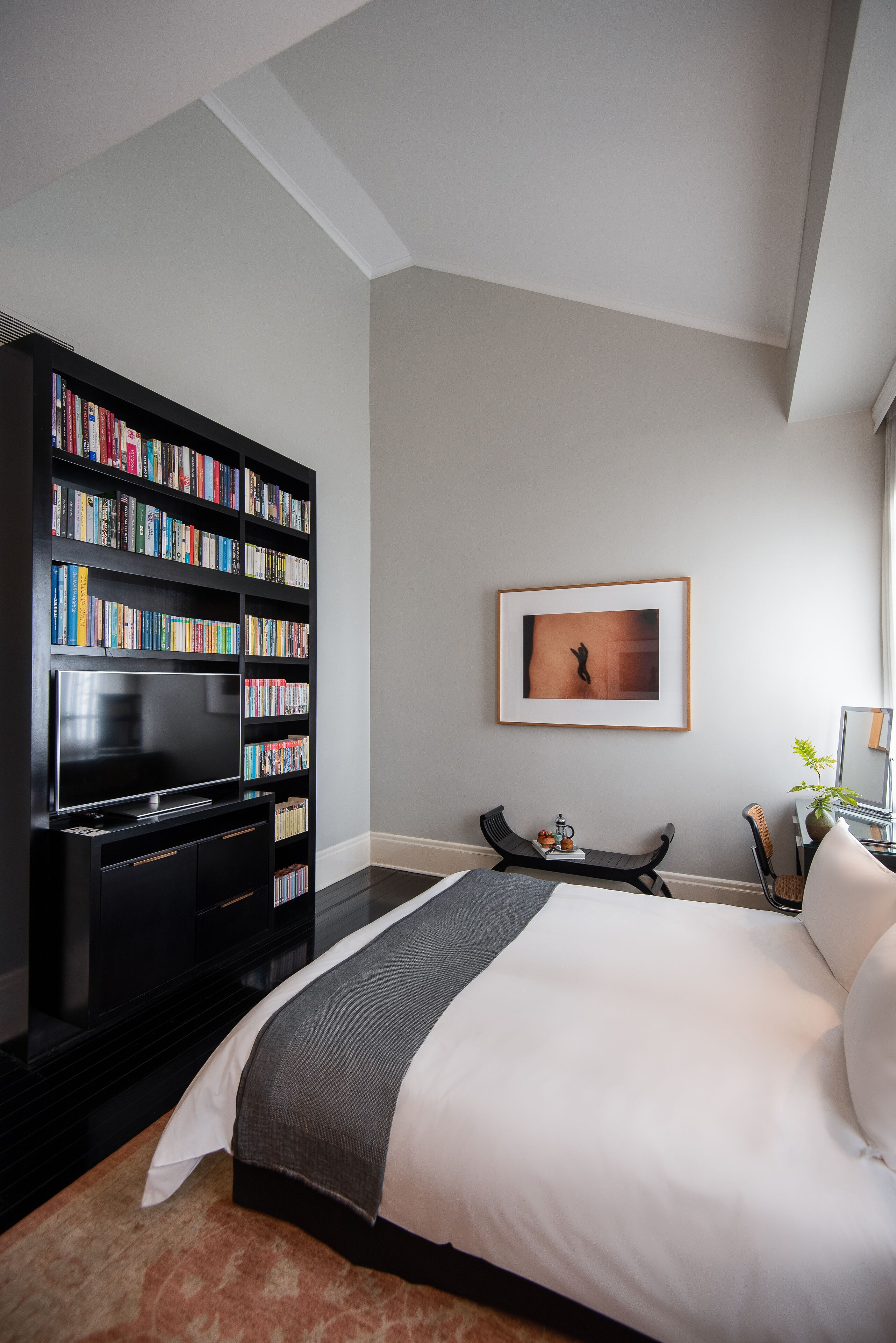 Ein modernes Hotelzimmer mit einem großen Bett, einer Bücherwand, einem Flachbildfernseher und einem gerahmten Bild an der Wand.