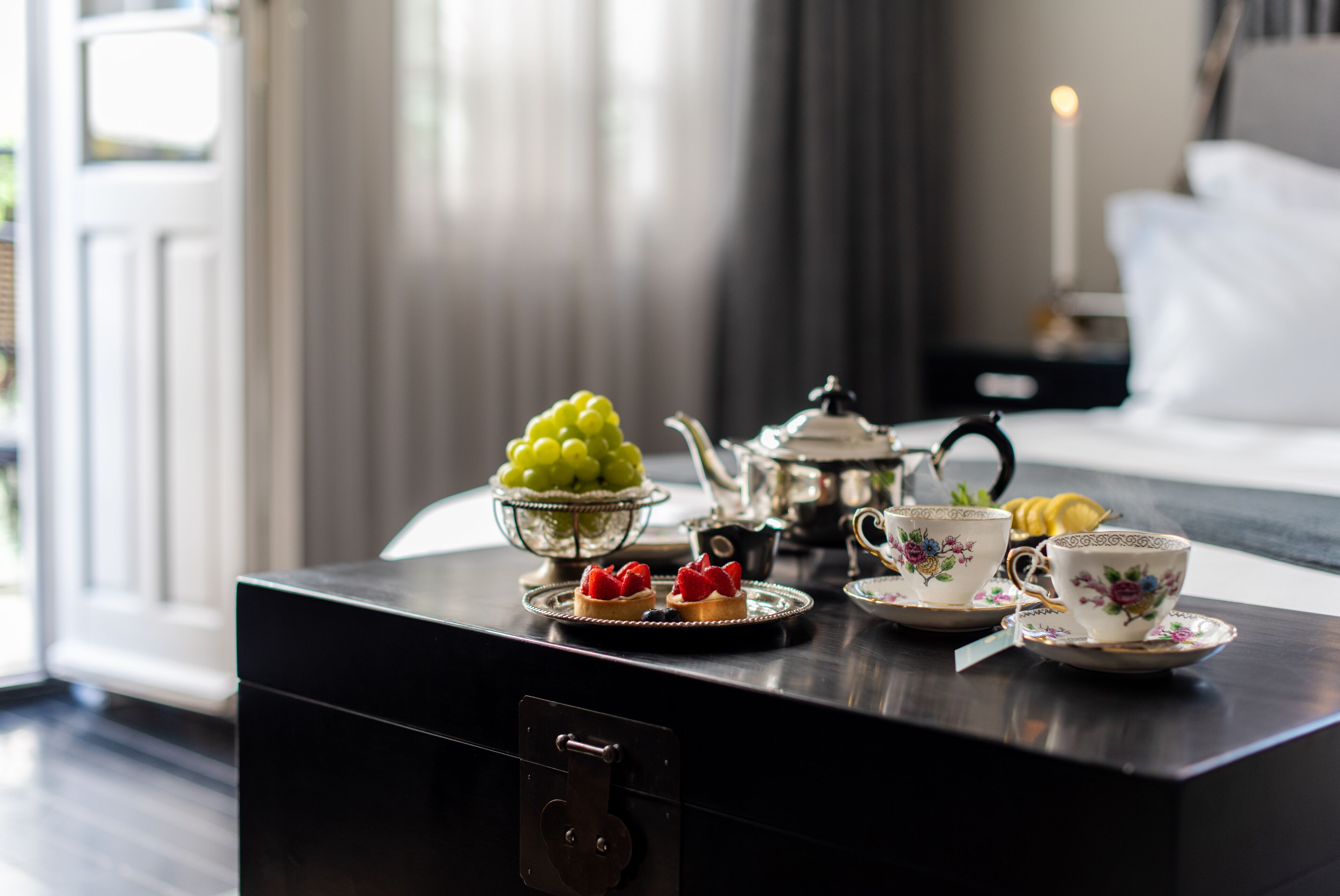 A neatly arranged table with a teapot, cups, and a bowl of fruit.