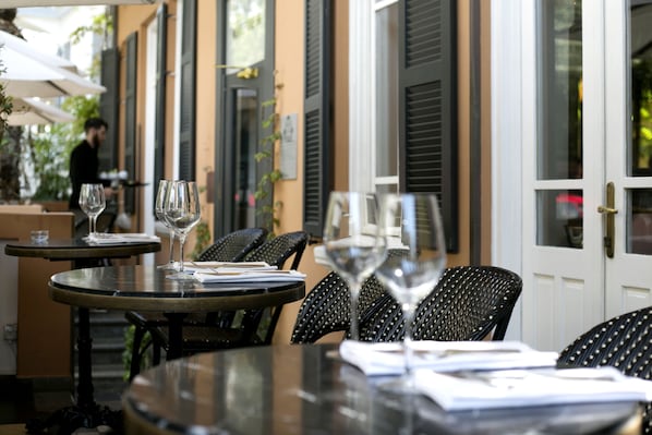Un café en plein air avec des tables et des chaises, dont certaines sont ornées de verres à vin.