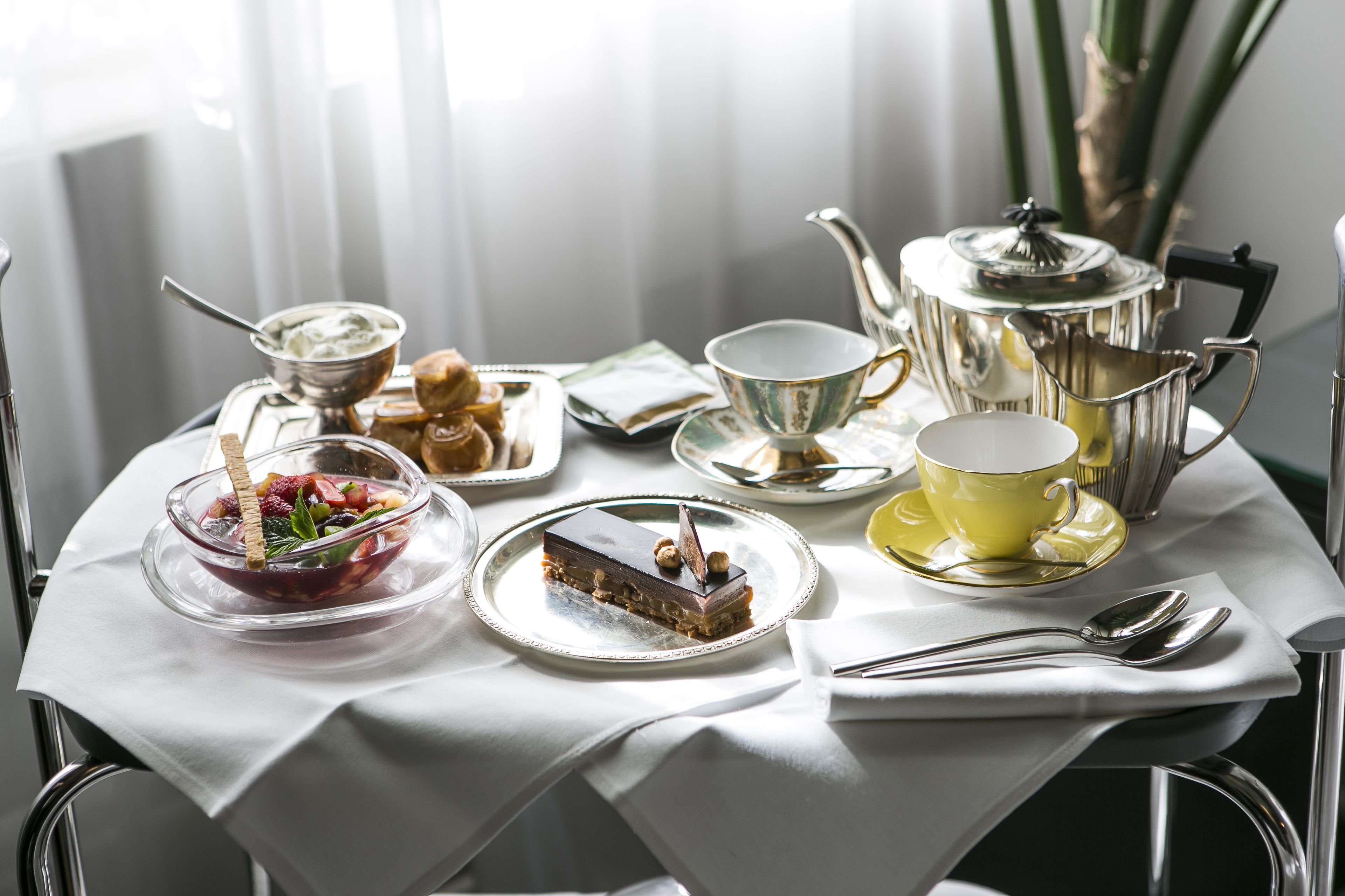 A table set with a variety of food items, including a dessert, a bowl of fruit, and a teapot.