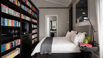 Un dormitorio ordenado con una cama grande, una estantería llena de libros y una mesita de noche con una lámpara y una planta.
