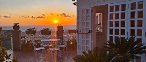 A patio with outdoor seating and a view of the sunset over the sea.