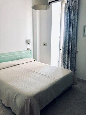 Una habitación sencilla y limpia con una cama, una lámpara y una ventana con cortinas.