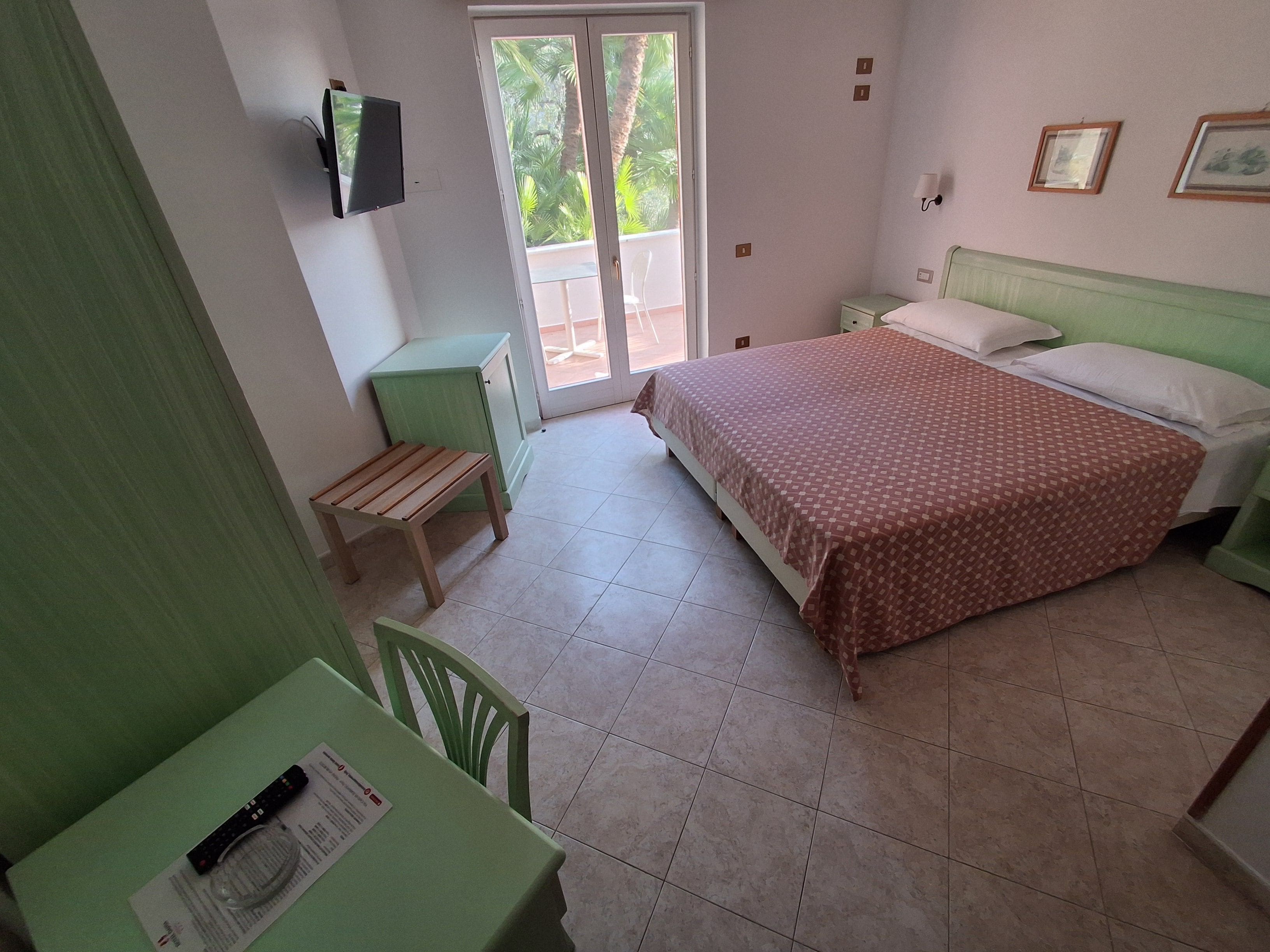 Ein Schlafzimmer mit einem Bett, einem Schreibtisch mit Stuhl, einem kleinen Schrank und einem Fernseher an der Wand.