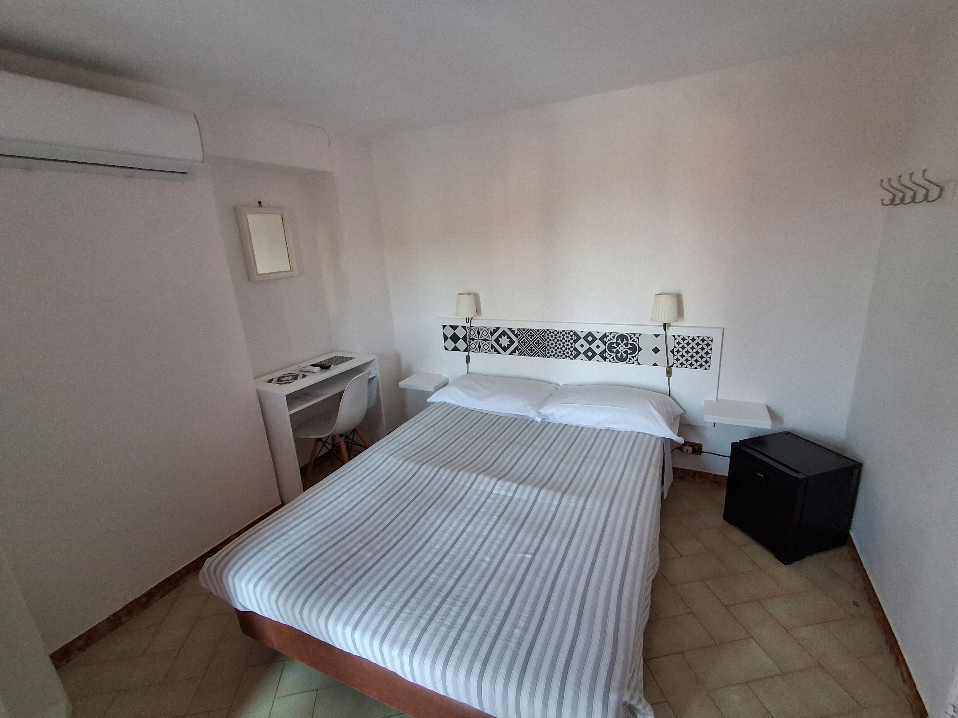 A bedroom with a bed, desk, chair, bedside tables, and a wardrobe.