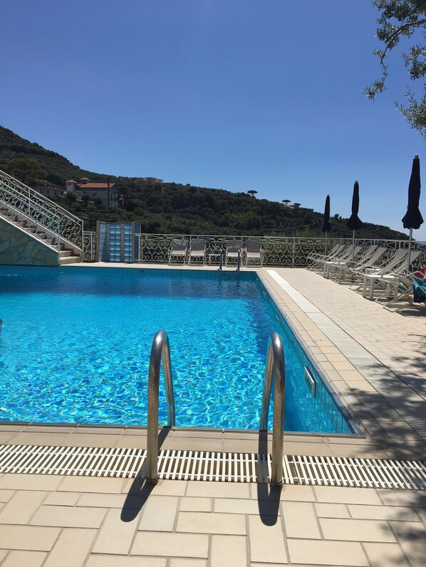 Una piscina con agua cristalina azul, rodeada por un borde de baldosas y barandillas de metal.