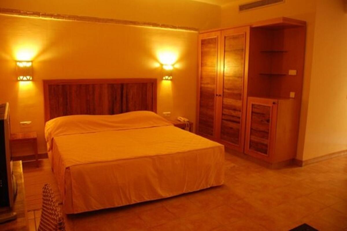 A bedroom with a large bed, wooden headboard, two bedside lamps, and a wardrobe.